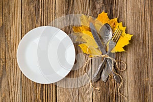 Thanksgiving dinner plate with fork, knife and autumn leaves on rustic wooden table background. Top view, copy space