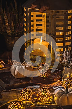 Autumn terrace in night with white pumpkins, lights and dried leaves