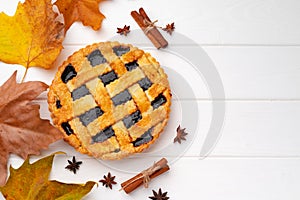 Autumn thankgiving pie on white wooden board decorated with dry leaves and cinnamon sticks