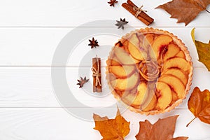 Autumn thankgiving pie on white wooden board decorated with dry leaves and cinnamon sticks