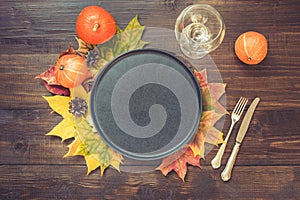 Autumn and Thanksgiving day table setting with fallen leaves, pumpkins, black platter and vintage cutlery on brown