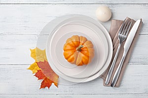 Autumn Thanksgiving table setting for dinner with plate, knife, fork decorated pumpkins and maple leaves. Top view