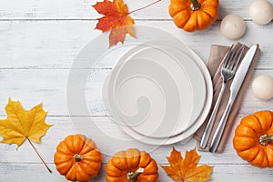 Autumn Thanksgiving table setting for dinner with plate, knife, fork decorated pumpkins and maple leaves. Top view