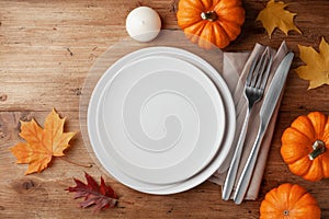 Autumn Thanksgiving table setting for dinner with plate, knife, fork decorated pumpkins and maple leaves. Top view