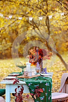 Autumn themed holiday table setting arrangement for a seasonal party, cups, apples, candles, field flowers.