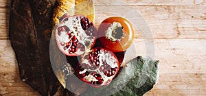 Autumn themes image with brown and yellow leaves and red pomegranate on a woode tabl viewed from above in top composition. Concept