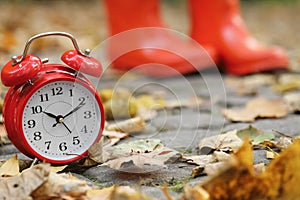Autumn time. Alarm clock and rainboots in park, selective focus