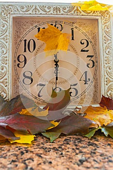 Autumn time change. Fallen leaves and clock on stone background.