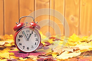 Autumn time change. Fallen leaves and old alarm clock on rustic wooden background. Autumn leaves. Autumn time