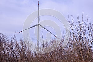 Autumn tree branches against the background of a wind turbine blade and cloudy sky