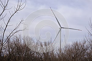 Autumn tree branches against the background of a wind turbine blade and cloudy sky