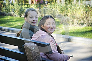 In autumn, two girls sit on a bench in the park