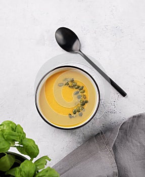 Autumn vegetarian pumpkin soup with cream and seeds on white  background with fresh herbal and spoon