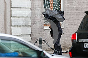 A man with an umbrella is hiding from strong winds and rain