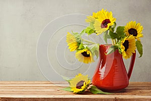 Autumn wallpaper. Sunflowers in red vase on wooden table