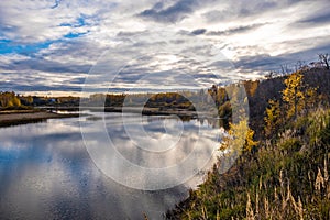 Autumn water landscape with reflection in the river of cloudy sky and yellow trees on the shore