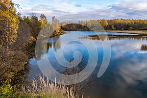 Autumn water landscape with reflection in the river of cloudy sky and yellow trees on the shore