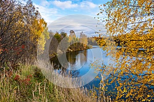 Autumn water landscape with reflection in the river of cloudy sky and yellow trees on the shore