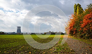 Autumn windy day in Germany, cloudy sky yellow leaves falling from trees standing near a dirt road and farmland. In the distance,