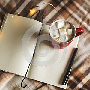 Autumn and winter background with notebook, pen, garland, mug of cocoa, coffee or hot chocolate with marshmallow on