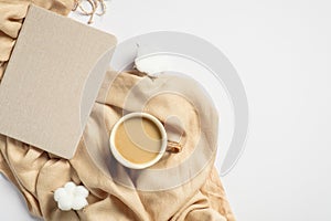 Autumn or winter flat lay composition. Cup of coffee, beige scarf, paper notebook, cotton on white background. Hygge style, cozy