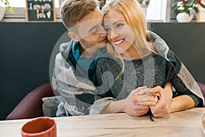 Autumn winter portrait of young embracing couple. Young man and woman in cafe under warm woolen blanket drinking coffee tea, happy