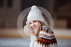 Autumn, Winter portrait: Young smiling woman dressed in a warm woolen cardigan, gloves and hat posing outside.