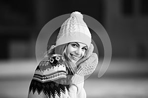 Autumn, Winter portrait: Young smiling woman dressed in a warm woolen cardigan, gloves and hat posing outside. Black and