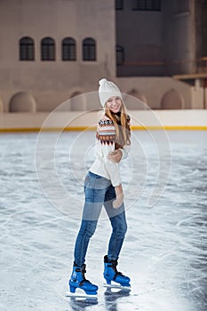 Autumn, Winter portrait: Young smiling woman dressed in a warm woolen cardigan, gloves and hat posing outside in skating