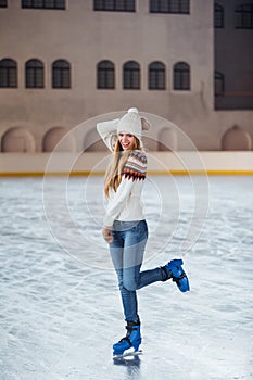 Autumn, Winter portrait: Young smiling woman dressed in a warm woolen cardigan, gloves and hat posing outside in skating