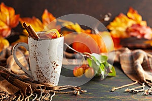 Autumn or winter spice tea in mug with seasonal fruits, berries, pumpkin and leaves on wooden table