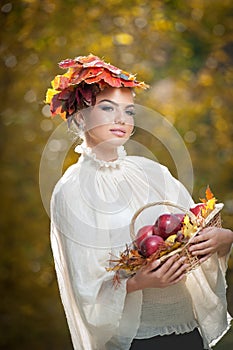 Autumn Woman. Beautiful creative makeup and hair style in outdoor shoot . Girl with leaves in hair holding a basket with apples