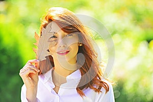 Autumn woman with bright orange hair. Cheerful smiling ginger woman holding fall oak leaves. Healthy and natural woman