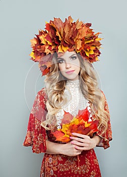 Autumn woman in fall leaves crown holding red leaves in hands on gray background. Pretty model with blonde curly hair and makeup