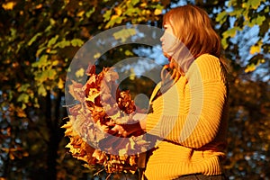 Autumn woman holding dry leaves. Volunteer rakes and grabs a small pile of yellow fallen leaves in the autumn park