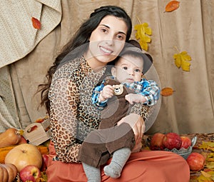 Autumn woman with little boy on yellow fall leaves, apples, pumpkin and decoration on textile, happy family and country concept