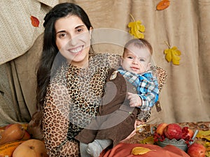 Autumn woman with little boy on yellow fall leaves, apples, pumpkin and decoration on textile, happy family and country concept