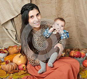 Autumn woman with little boy on yellow fall leaves, apples, pumpkin and decoration on textile, happy family and country concept