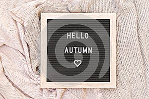 Autumnal Background. Black letter board with text phrase Hello Autumn lying on white knitted sweater. Top view, flat lay