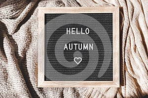 Autumnal Background. Black letter board with text phrase Hello Autumn lying on white knitted sweater. Top view, flat lay.