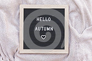 Autumnal Background. Black letter board with text phrase Hello Autumn lying on white knitted sweater. Top view, flat lay