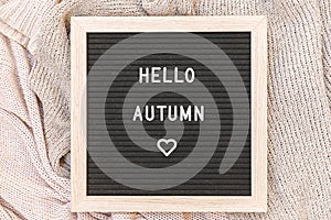 Autumnal Background. Black letter board with text phrase Hello Autumn lying on white knitted sweater. Top view, flat lay