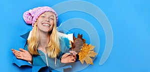 Autumnal mood. Smiling woman in knitted hat with autumn leaves looking through paper hole. Happy girl in autumn wear