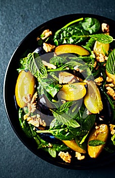 Autumnal plums and spinach salad with toasted walnuts, honey and mint leaves