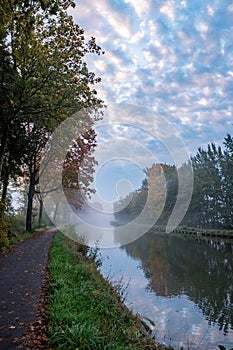 Autumnal Serenity: Canal Amidst Fall Foliage Under Cloud-Kissed Skies