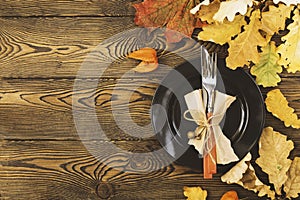 Autumnal table setting for Thanksgiving dinner. Empty plate, cutlery, colored leaves on wooden table. Fall food concept.