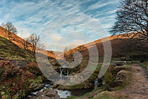 An autumnal waterfall and stone packhorse bridge at Three Shires