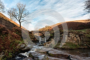 An autumnal waterfall and stone packhorse bridge at Three Shires