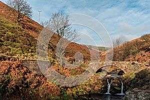 An autumnal waterfall and stone packhorse bridge at Three Shires