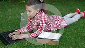 Available 5G internet everywhere. Schoolgirl girl in a red shirt on green grass in the park near the laptop. technology